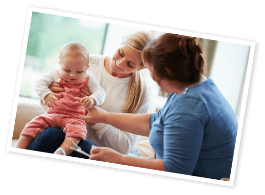 Photo of a younger woman holding a baby on her knee while an older lady reaches out toward the baby